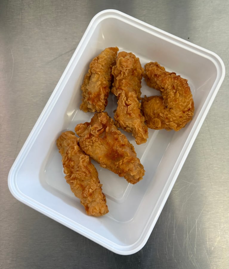 Six pieces of golden fried chicken in a white foam takeout container on a stainless steel surface