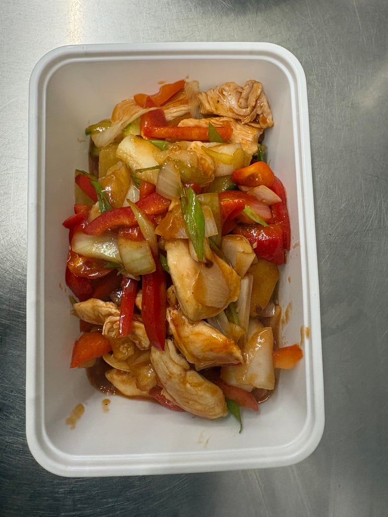 Stir-fried chicken and vegetables with bell peppers, onions, and green onions in a white container