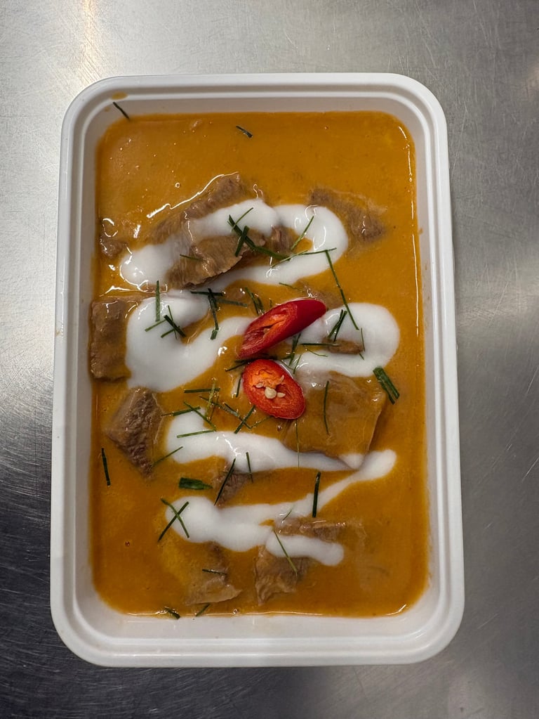 White squid in spicy curry sauce with fresh herbs and sliced red chili in a plastic container