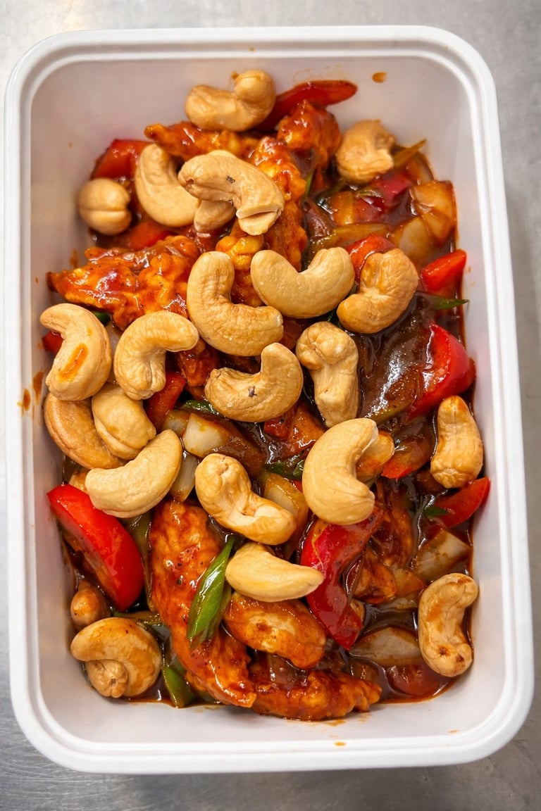 Stir-fried cashews and red bell peppers with meat in a white rectangular takeout container