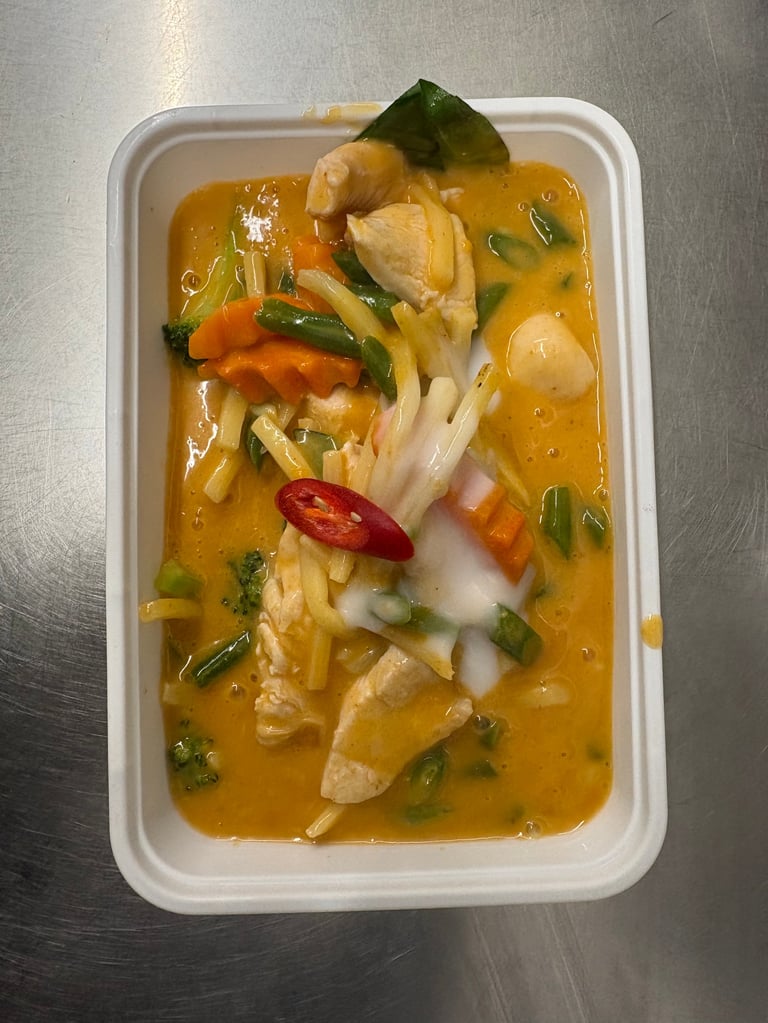 Bowl of Thai curry soup with chicken, noodles, mushrooms, and green onions in creamy yellow broth.