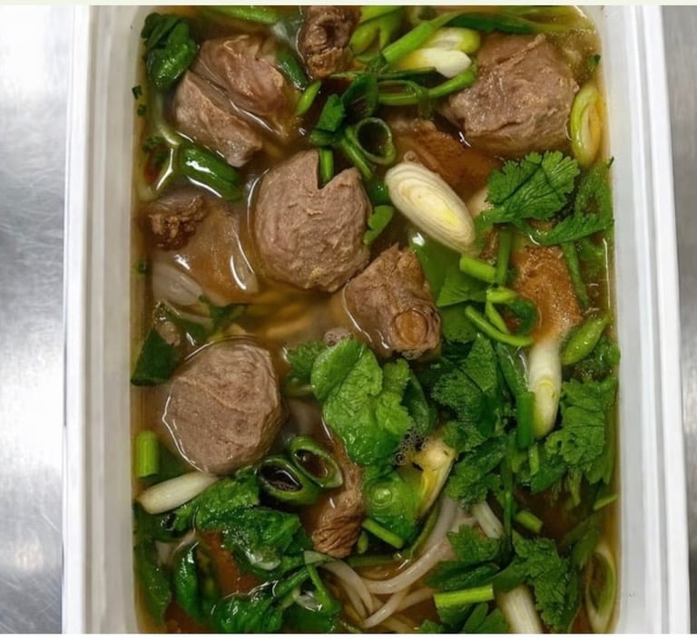 Bowl of Vietnamese pho soup with beef meatballs, fresh greens, and noodles in broth