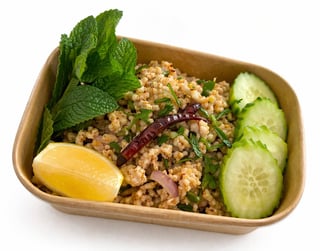 Healthy meal in cardboard container with quinoa, fresh cucumber slices, lemon wedge, and mint leaves