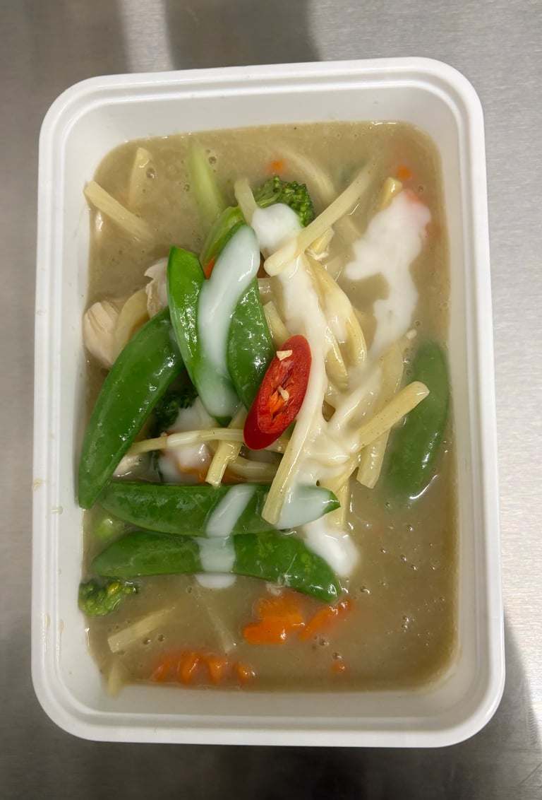 Bowl of Asian noodle soup with bok choy, mushrooms, red chili, and julienned vegetables in clear broth in a white takeout container