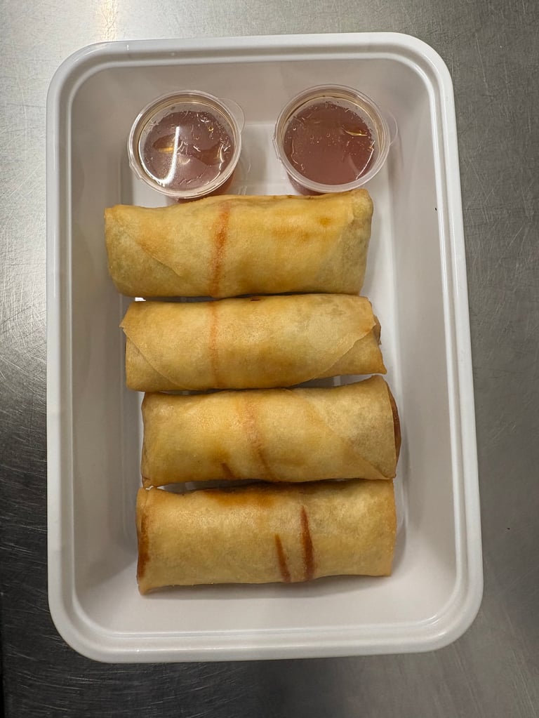 Four golden fried spring rolls arranged in a white takeout container with two small cups of dipping sauce