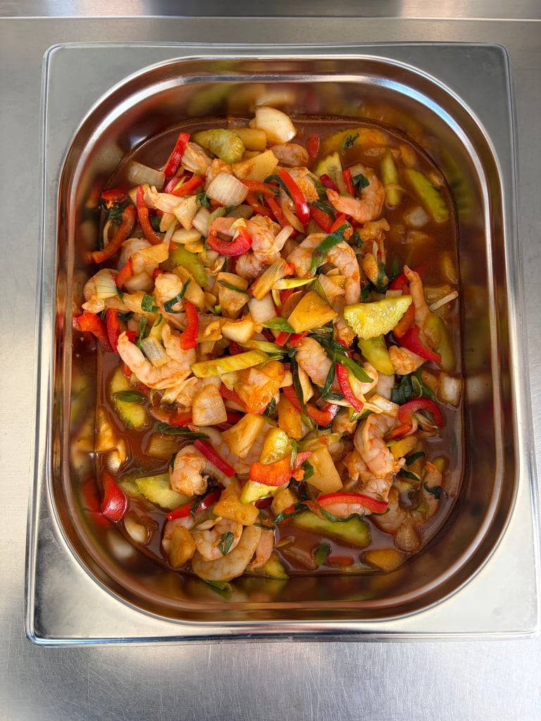 Metalen pan met in blokjes gesneden garnalen, aardappelen, rode pepers en groene uien in een hartige saus