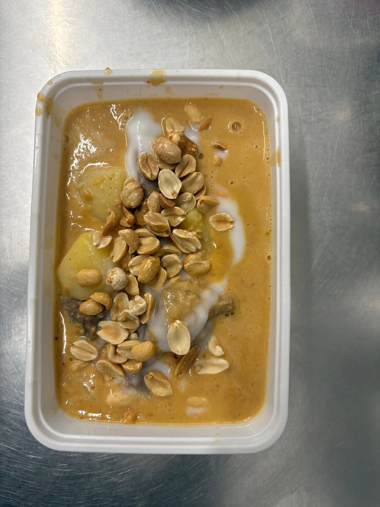 Peanut butter in a white plastic container with peanuts and a swirl of white cream on top